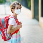 Nine years old girl goes back to school wearing a mask and a schoolbag
