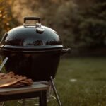 Kugelgrill mit Grillzange, Grillhandschuhen und Anzündkamin im Garten bei Abendlicht