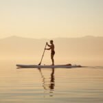 Stand-Up-Paddler mit Leash am Knöchel und Sicherheitsboje paddelt auf einem ruhigen See